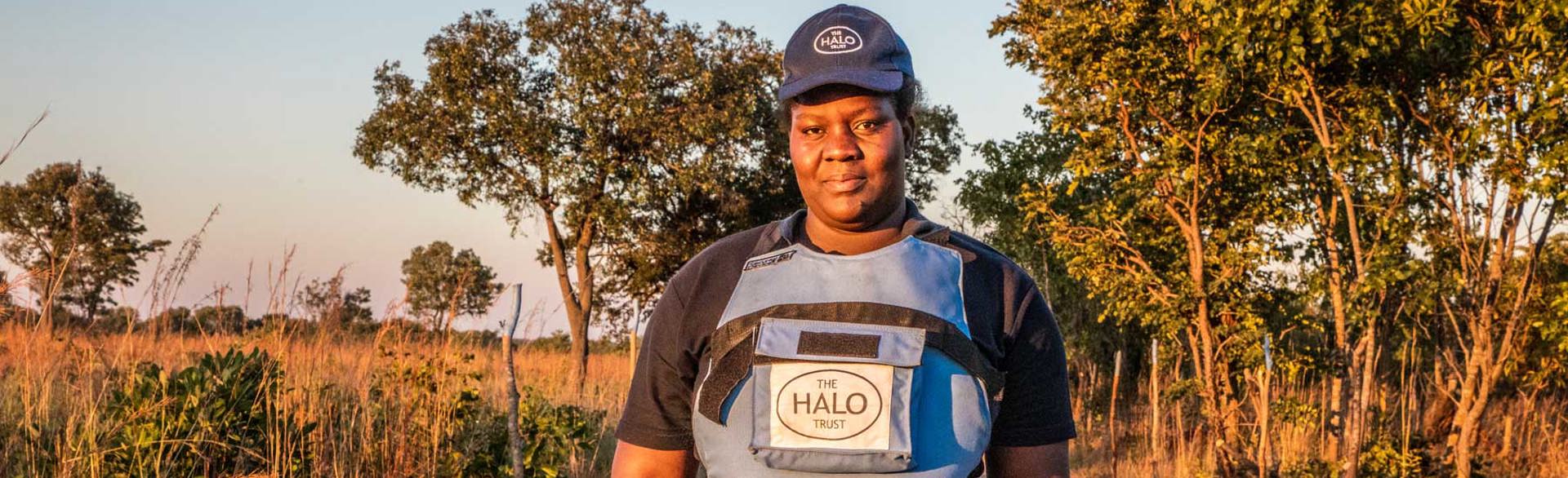 A female deminer poses at sunset whilst wearing HALO uniform in a field