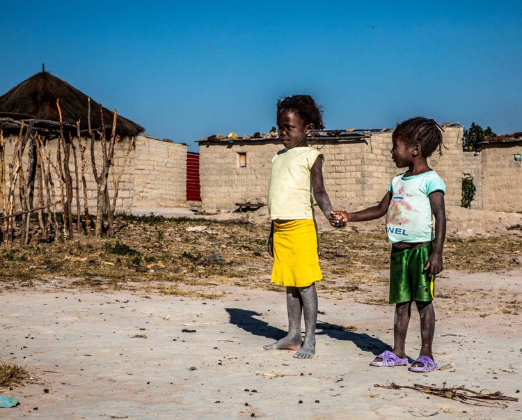 Two children hold hands outside of a house in the village of Lusserei Village, Angola