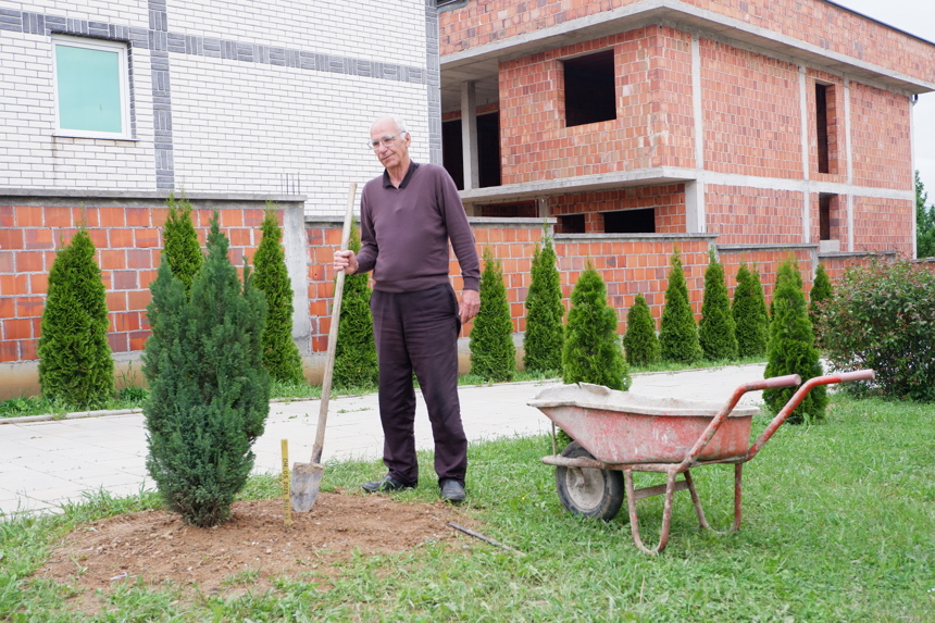 A man plants a tree outside of a house in Arllat village in Kosovo