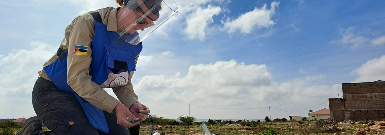 HALO staff member wearing a visor and PPE holds a wire while kneeling on sandbags