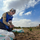 HALO staff member wearing a visor and PPE holds a wire while kneeling on sandbags