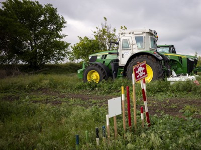 A large agricultural machine stands in the middle of a field behind a landmine warning sign.