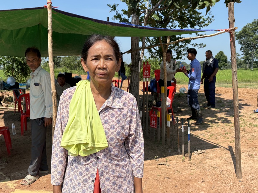 Po Sarin stands outside a sun tent with mine warning signs behind her