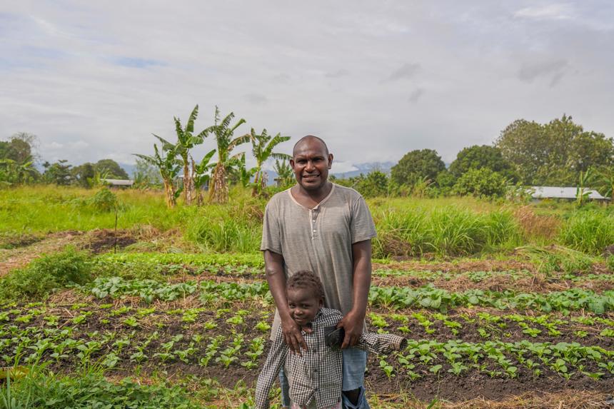 A man and his young son stand in front of their green garden