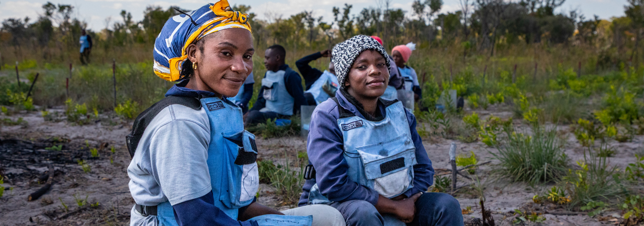 HALO deminers sit in a muddy field in Cuito Cuanavale, Angola wearing PPE