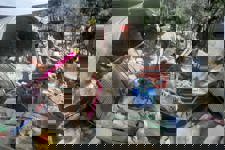 3 boys stand amongst rubble and home supplies in Khost