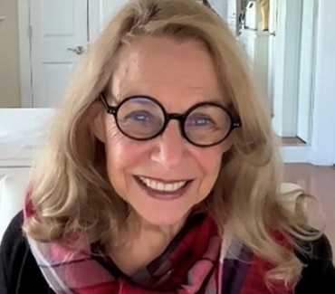 Mitzi Perdue, wearing large round glasses and a red-patterned scarf