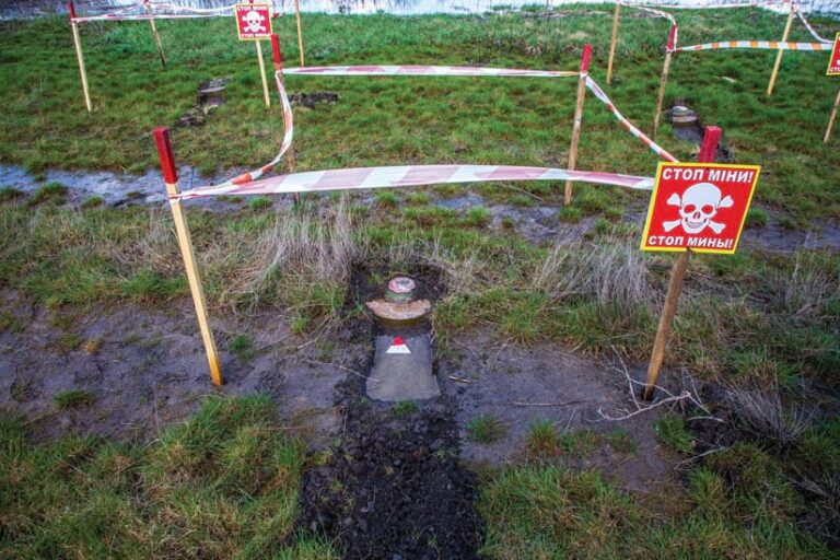 Close-up of a fenced-off landmine, surrounded by signs and tape in a rural minefield