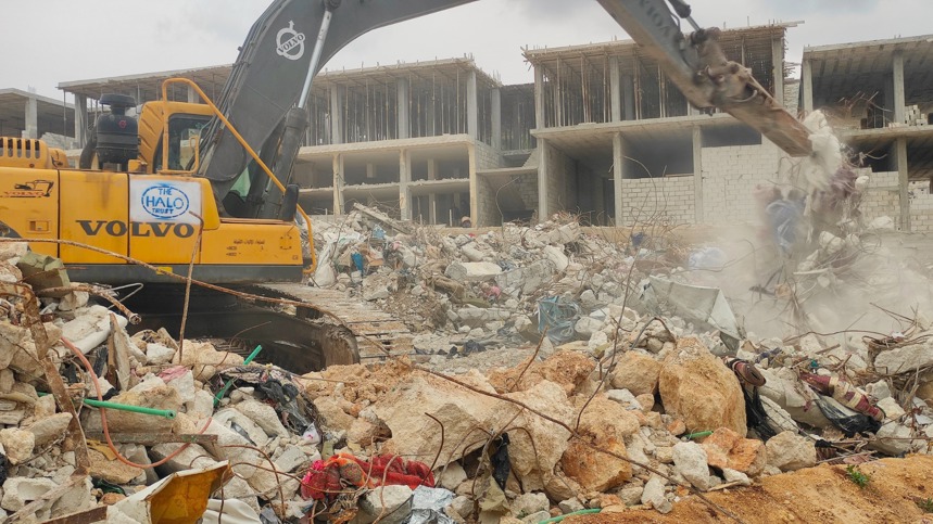 Excavator moves debris from a large pile of rubble outside