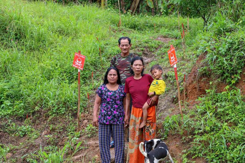 Cheng Seang and his family stand on grassy land marked with mine warnings