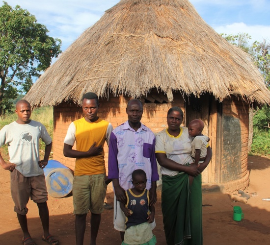 Miriam poses with their family outside a hut