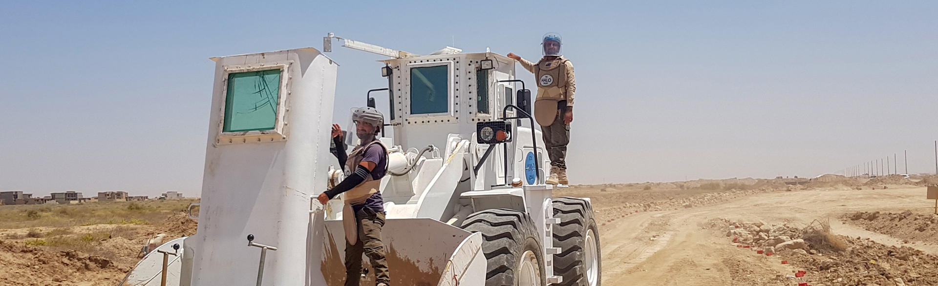 HALO staff ride a front loader used for mechanical clearance on a dusty track