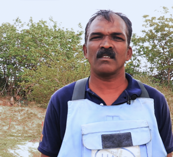 Sureshkumar, HALO Deputy Area Supervisor, stands in a field while wearing PPE