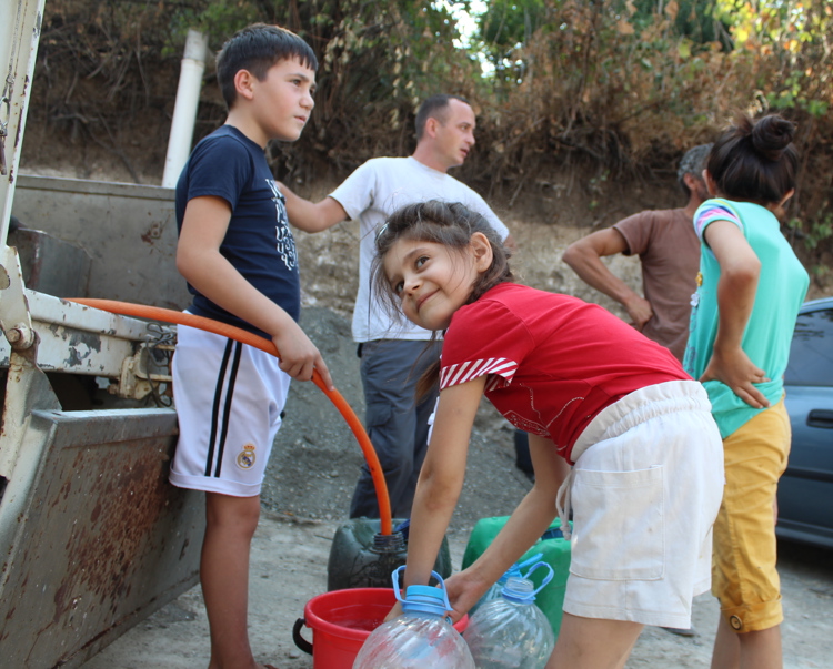 Kids with adults filling up buckets and bottles of water