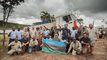 HALO and National Geographic Staff stand in front of HALO vehicles and hold the National Geographic flag