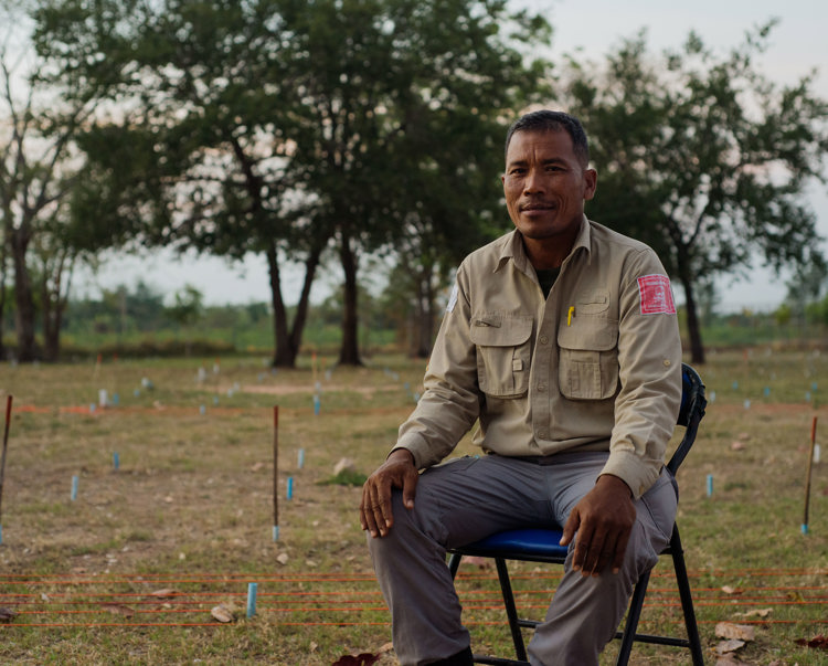 Un Ek, Head of Training and Quality Assurance in Cambodia, sits on a chair in a marked minefield