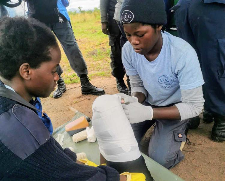 A person lays down as two women bandage their knee for paramedic refresher training