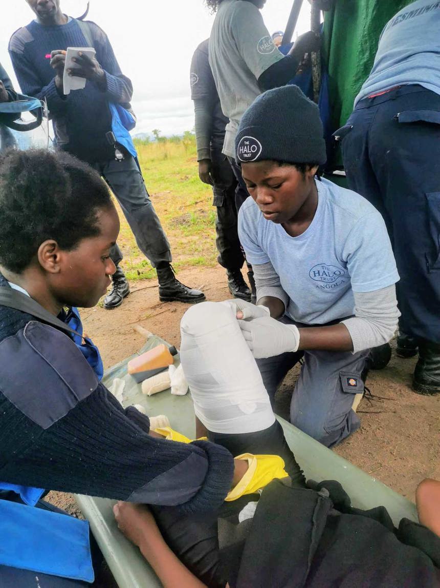 A person lays down as two women bandage their knee for paramedic refresher training