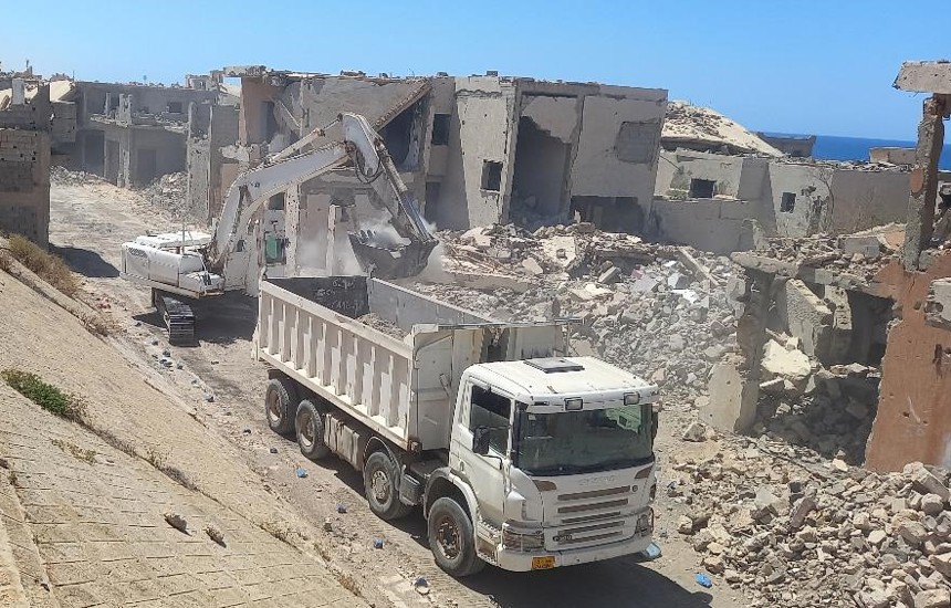 An armoured digger scoops rubble into the back of a lorry in Sirte, Libya