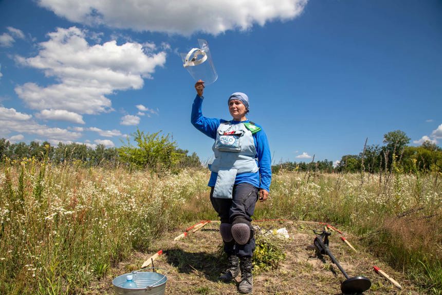 A HALO deminer holds her visor up in a grassy minefield in Ukraine