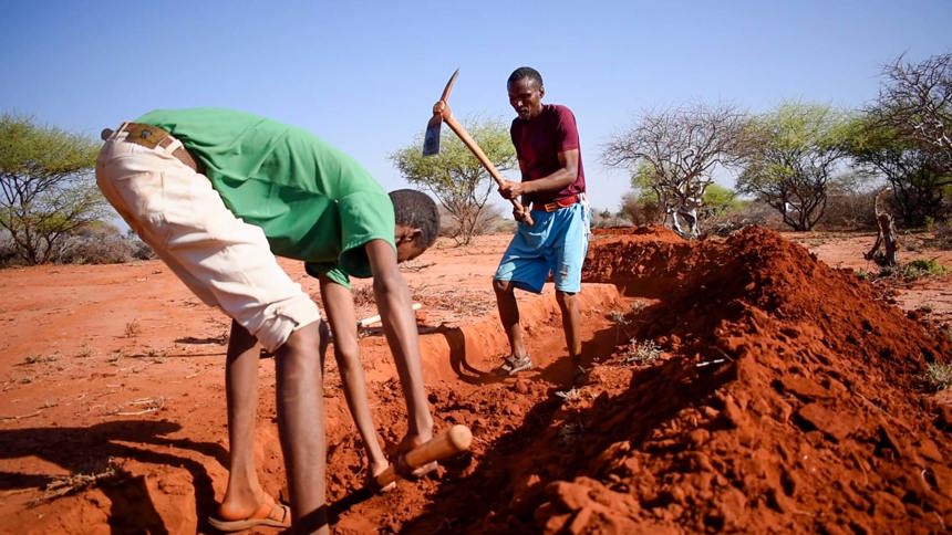 Two men use tools to dig into the ground forming a ridge line