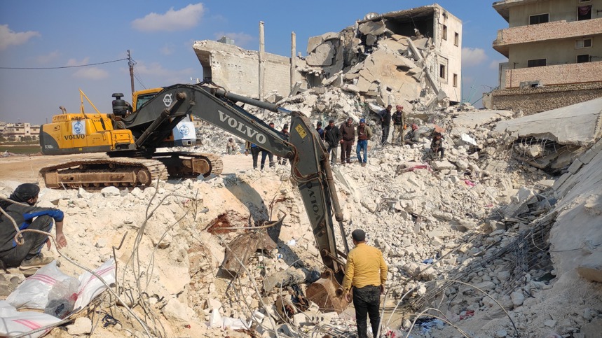 Men stand around an excavator in Al-Atareb city being used for rubble removal