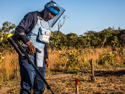 A male deminer uses a metal detector in a rural field