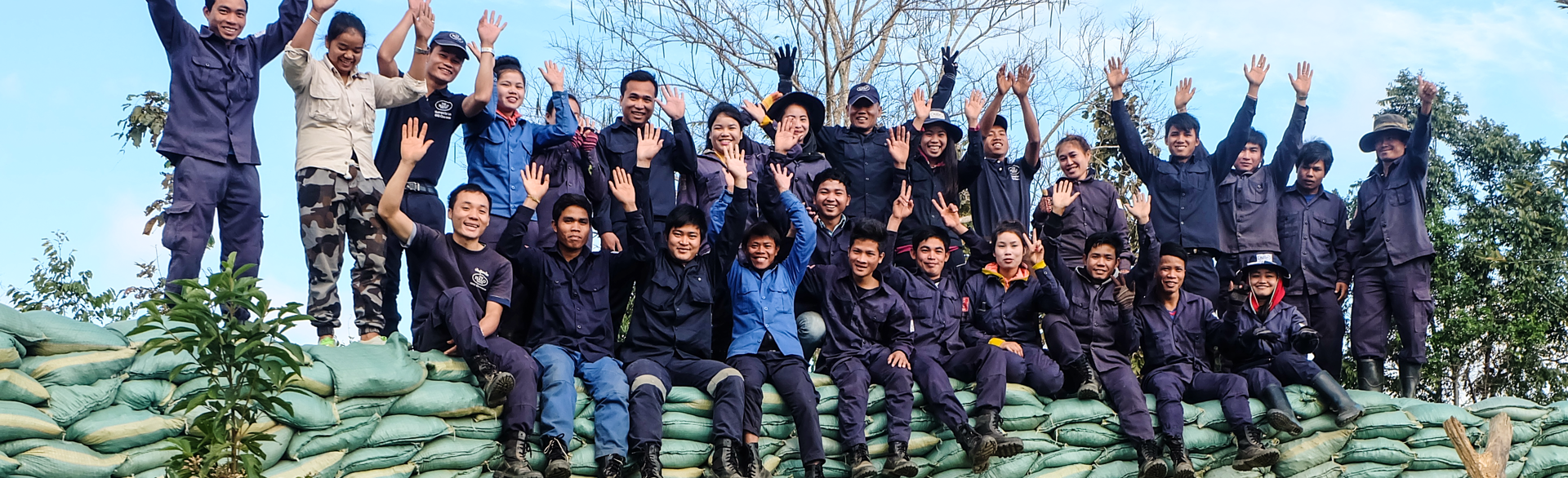 Deminers in Laos smile and wave on top of a large pile of sandbags