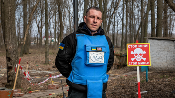 A deminer poses next to a mine warning sign in the forest