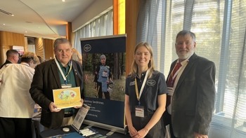Three people pose for a photo at an exposition booth.