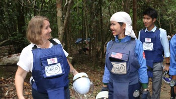 Two HALO staff smile together wearing uniforms with a UK aid badge and American flag