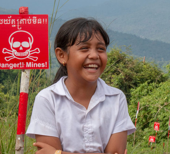 A girl sits in front of a danger mines sign in a field in Cambodia