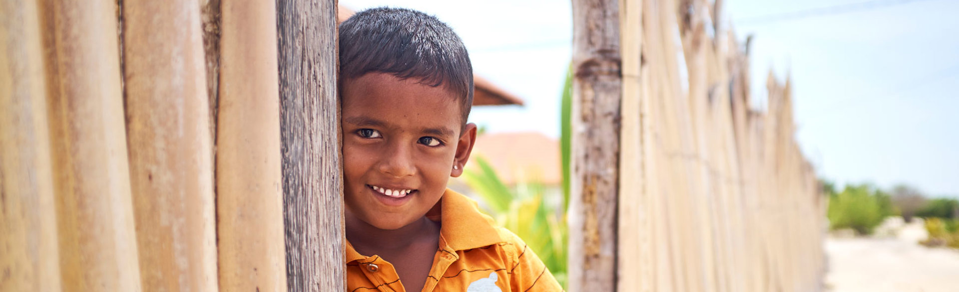 A young boy smiles for a photo next to a fence in Sri Lanka