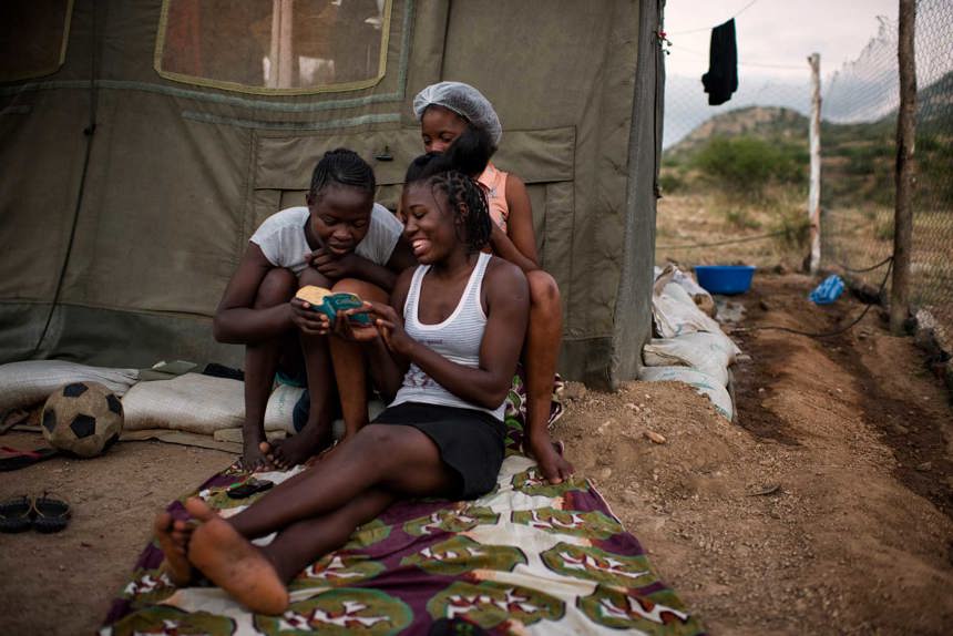 Women sit down to read and do hair outside the camp in Angola