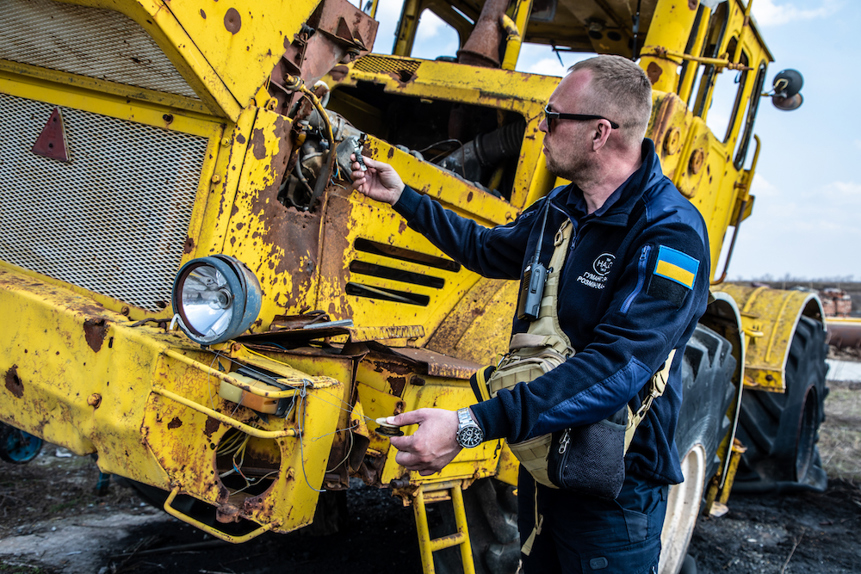 A HALO Staff member stands next to a tripwire rigged to a tripwire on a bright yellow tractor in Ukraine