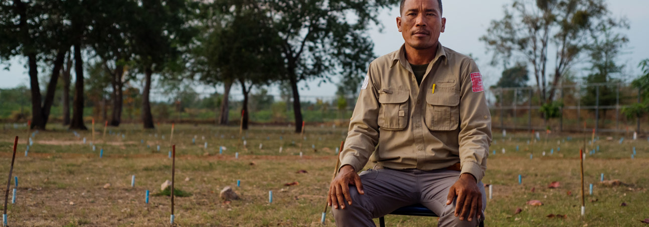 Un Ek, the Head of training in Cambodia, sits in a marked minefield