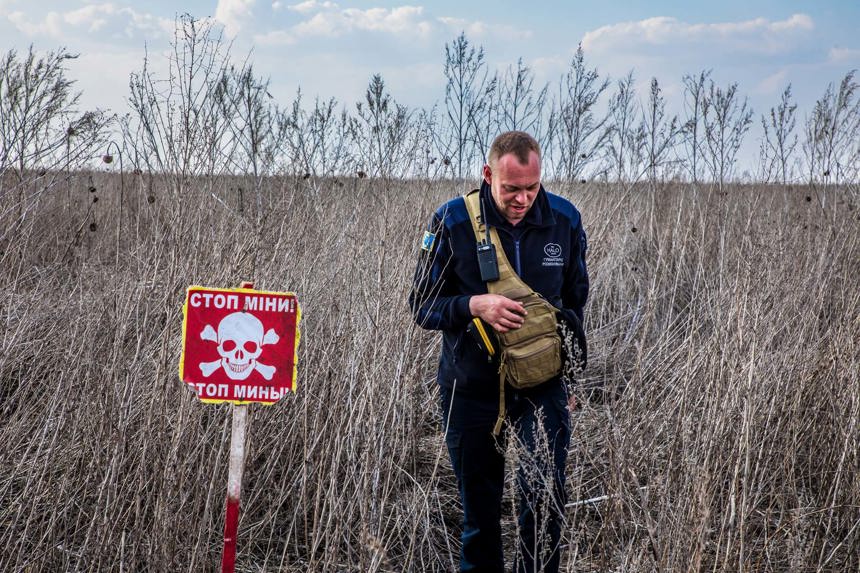 A HALO staff member walks through tall grass next to a red danger mines sign in Ukraine