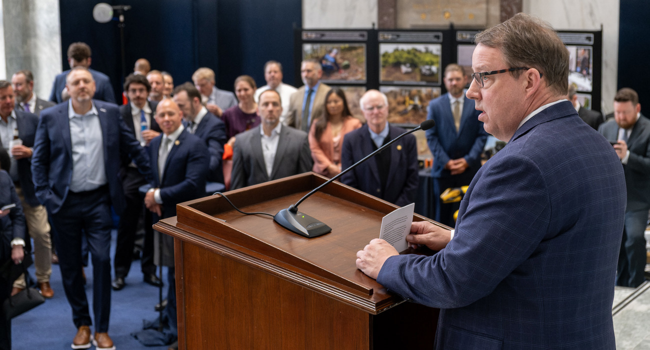 A man stands at the event podium speaking to a full room