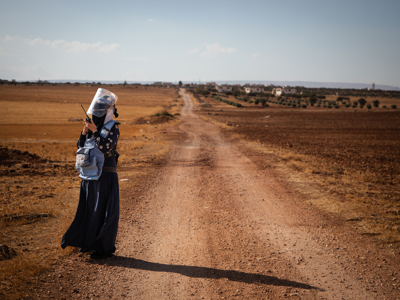 Deminer Hiba talks on a portable radio in front of a long stretch of dirt road.