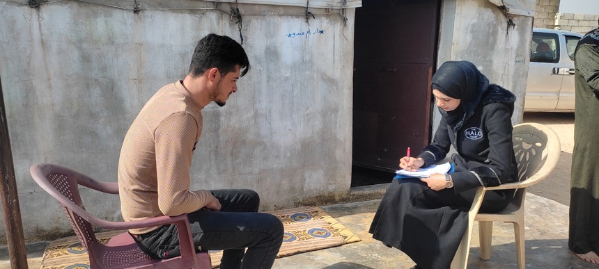 A HALO staff member sits with a man outside while writing on her clipboard