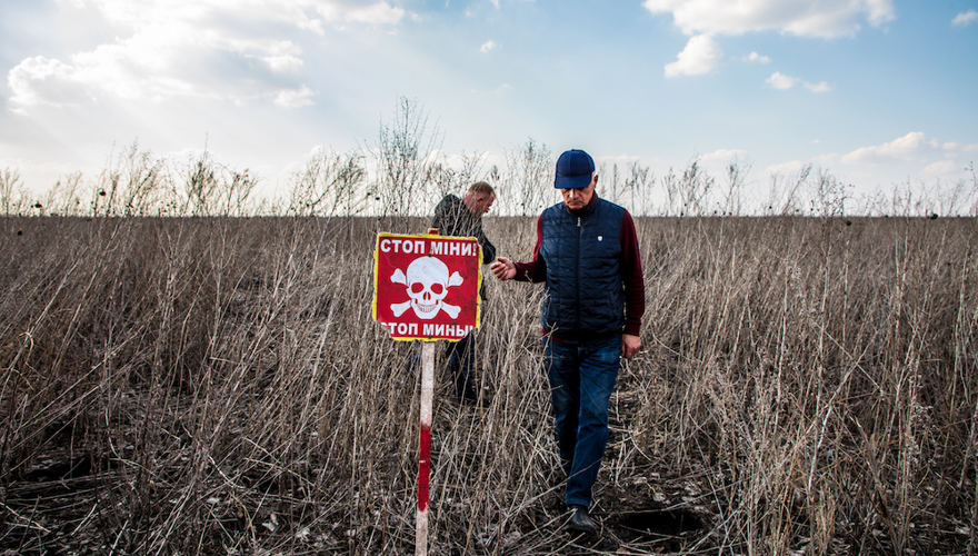 Two men walk in a agricultural field with a red mine warning sign