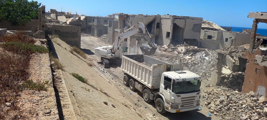 An excavator moves rubble from damaged buildings on the side of the street