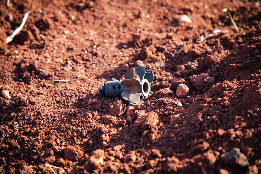 The tail of a 82mm mortar lays on the surface of the red soil.