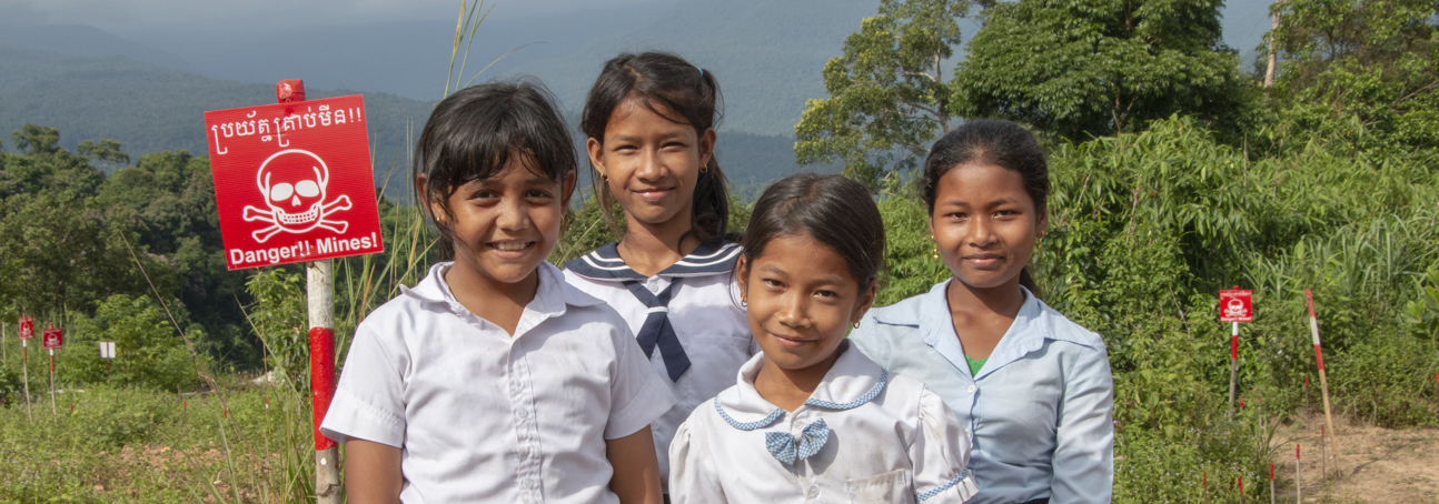 Four children pose in front of a minefield with warning signs in Cambodia