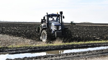 A tractor sits parked on a freshly planted farm field under a clear sky