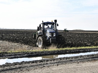 A tractor sits parked on a freshly planted farm field under a clear sky