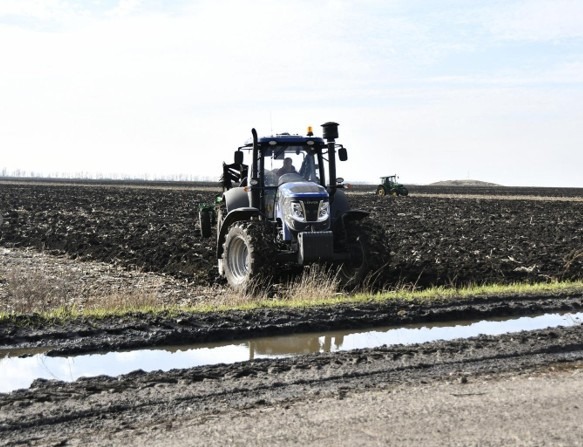 A tractor sits parked on a freshly planted farm field under a clear sky
