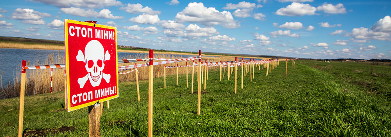 A red danger mines sign in front of fenced off land containing landmines next to a lake in Ukraine