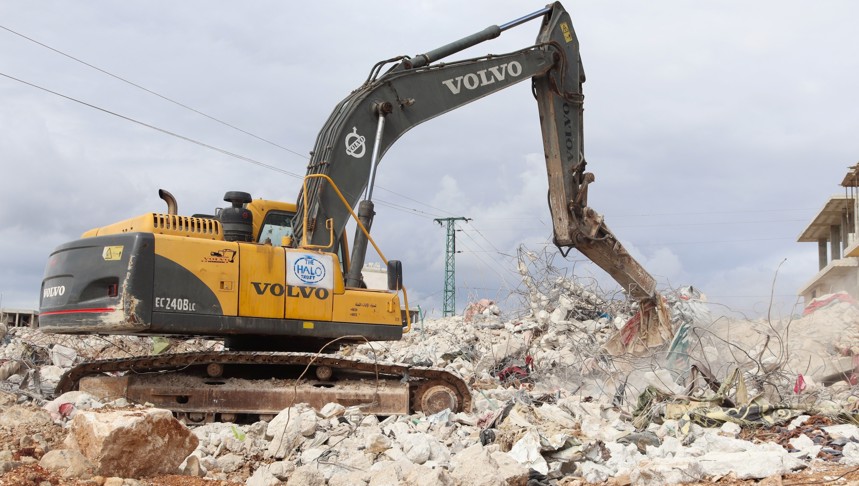 Excavator picks up debris from a large pile of rubble outside
