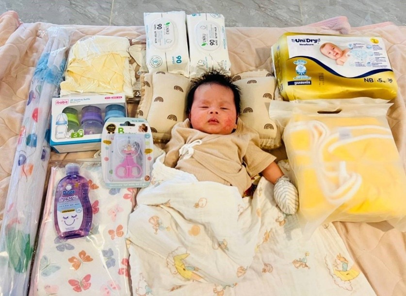 A baby lays on a soft mat with a blanket and maternal care items around them
